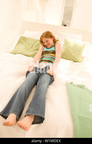 Teenage girl (14-16) sitting on bed, mettre sur un jean Banque D'Images