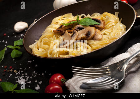 Tagliatelles aux champignons frais et basilic dans une casserole sur fond noir Banque D'Images