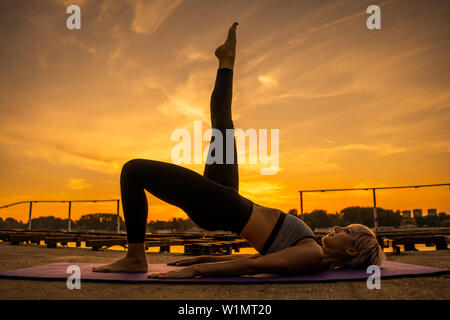 Woman practicing yoga dans le coucher du soleil. Setuasana / poser demi-pont Banque D'Images