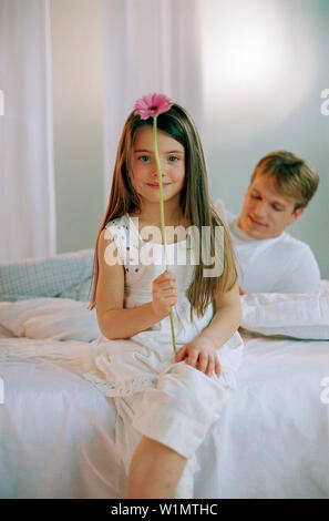 Fille avec Gerbera sur lit avec père, portrait Banque D'Images