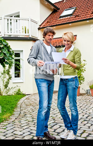 Jeune couple looking at documents in front of a house, Hambourg, Allemagne Banque D'Images