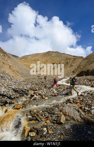 Une jeune femme et un jeune homme sautant au dessus d'un ruisseau sur le chemin de Nar sur Teri Tal à Mustang, Népal, Himalaya, Asie Banque D'Images