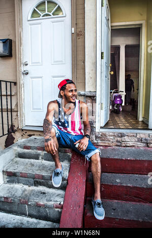 Portrait of young African American man dans un drapeau américain shirt siège en face de son domicile à Kensington Philadelphia Banque D'Images