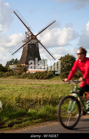 Vélo Femme, moulin en arrière-plan, Oldsum, Foehr island, Schleswig-Holstein, Allemagne Banque D'Images