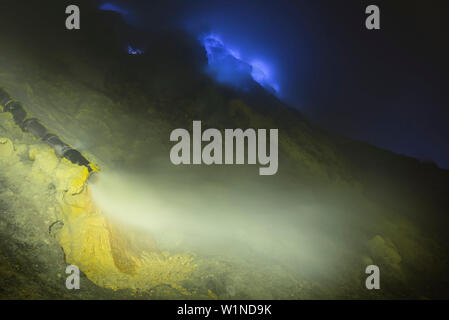 Soufre brûlant et flammes bleues du volcan Ijen de nuit. Le transfert du tuyau de gaz sulfureux chaud pour le refroidissement. Du dépôt de soufre sous forme solide, Eas Banque D'Images