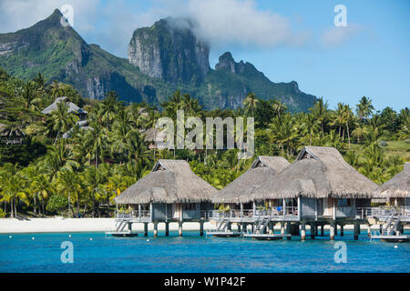 Bungalows sur pilotis sur pilotis d'un complexe de luxe sont éclipsées par les hautes montagnes en arrière-plan, Bora Bora, îles de la société, Polynésie Française, Banque D'Images