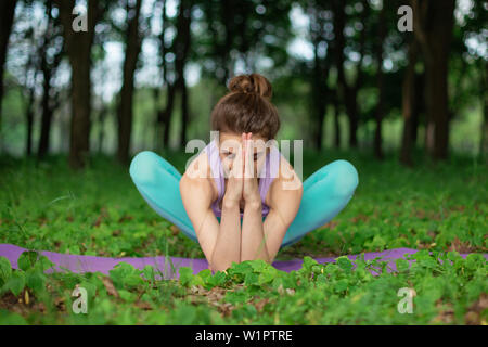 Brunette mince fille joue et exécute des sports belle et sophistiquée postures de yoga dans un parc d'été. La forêt verte sur l'arrière-plan. Femme exer Banque D'Images
