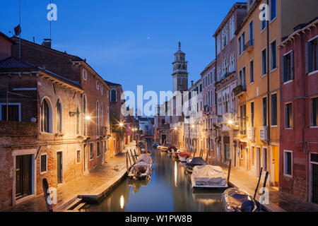 Maisons illuminées du Rio di San Barnaba avec la tour de l'église de Santa Maria dei Carmini et bateaux dans le bleu crépuscule, Dorsoduro, Venise, Ve Banque D'Images