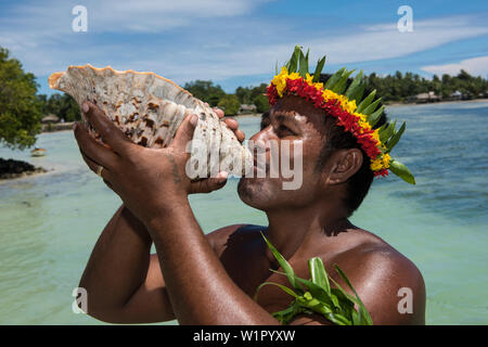 Un homme à la fleur et à feuilles souffle la couronne dans un grand coquillage d'annoncer l'arrivée de visiteurs d'une expédition en bateau de croisière, l'Atoll de Butaritari, Gil Banque D'Images