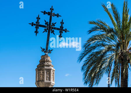 Une croix sur une colonne en pierre à côté d'un palmier en face de l'église, Selva, Majorque, Espagne Banque D'Images