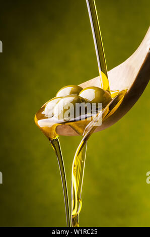 L'huile d'olive extra vierge flux sur un bol en bois plein d'olives vertes Banque D'Images