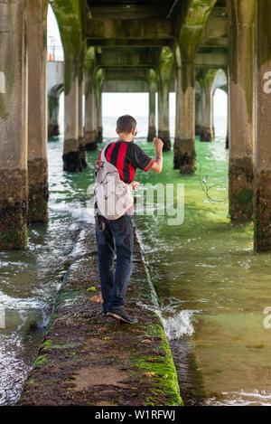 Boscombe, Dorset, Angleterre, Royaume-Uni, 3 juillet 2019, la météo : chaud soleil de l'après-midi sur la côte sud. Un metal detectorist tente sa chance dans la mer avec un aimant de pêche à marée basse sous la jetée victorienne restaurée. Crédit : Paul Biggins/Alamy vivre Banque D'Images