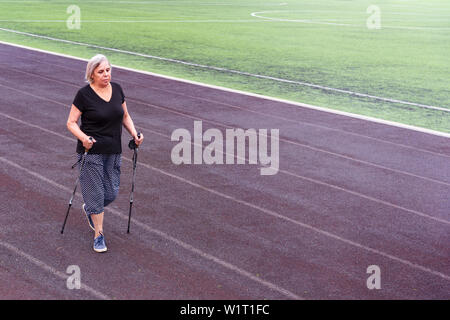 Vieille Femme faisant de la marche nordique dans un stade. Banque D'Images