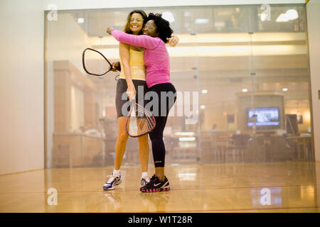 Two smiling women hugging en étant debout sur un court de racquetball. Banque D'Images