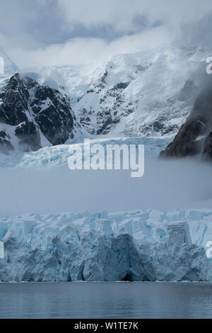 Coupes de brouillard par le milieu d'un glacier couronnée par les montagnes et les nuages, Paradise Bay (Paradise Harbour), Côte Danco, Terre de Graham, en Antarctique Banque D'Images