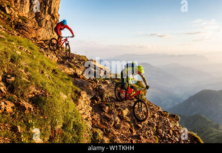 Deux hommes d'âge moyen en descendant une pente raide et rocheuse sur leur chemin de randonnée VTT, lumière du matin, de montagnes Wilder Kaiser en arrière-plan, Kir Banque D'Images