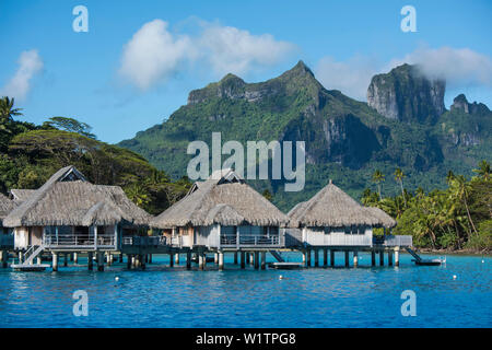 Bungalows sur pilotis sur pilotis d'un complexe de luxe sont éclipsées par les hautes montagnes en arrière-plan, Bora Bora, îles de la société, Polynésie Française, Banque D'Images