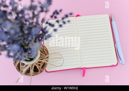 Regard sur le bloc-notes papier ouvert dans une couverture rose bouquet parfumé à la lavande sèche de avec de petites fleurs violettes dans un beau vase en céramique sur une pâte Banque D'Images