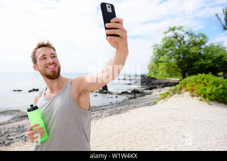 Homme remise en forme prendre lui-même des selfies après entraînement. Bon à prendre des jeunes adultes un auto-portrait photo avec son smartphone à l'appareil photo après l'exercice sur une plage pendant les vacances d'été. Banque D'Images