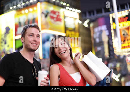 Heureux couple shopping plaisir sur New York city travel. Deux touristes appréciant groupe multiracial nuit sur Time Square, USA de boire du café et de la marche avec des sacs de shopping en été. Le mode de vie américain. Banque D'Images