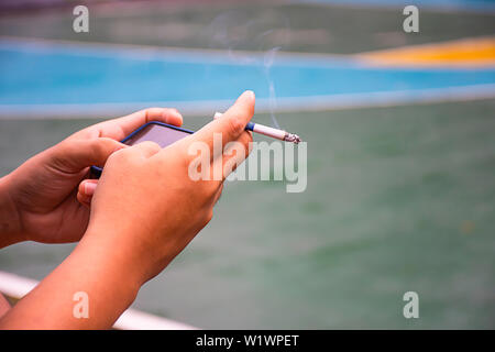 Main tenant une cigarette et d'un téléphone. Historique Le basket-ball Banque D'Images