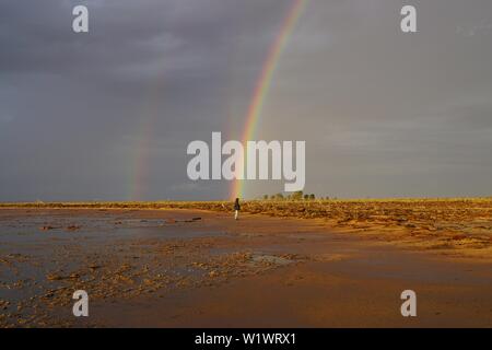 Petite Hooded figure à la fin d'un triple Arc-en-ciel sur le Lac Tyrrell Outback en Victoria, Australie Banque D'Images