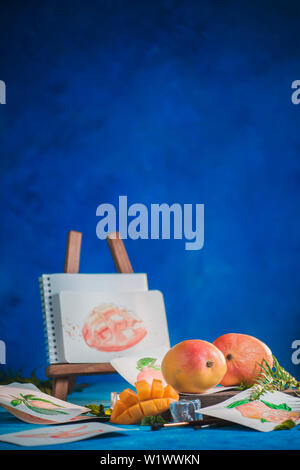 Fruits exotiques avec des croquis dans un milieu de travail de l'artiste. Mangue et orange sur un fond bleu avec copie espace Banque D'Images