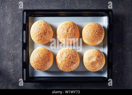 Des petits pains à burger chaud maison saupoudré de graines de sésame sur un plat allant au four Banque D'Images