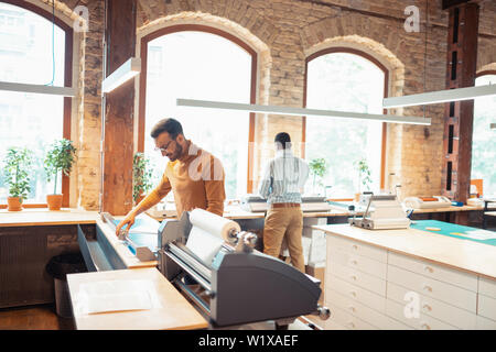 Homme debout. Brun col polo orange debout près de technique d'impression moderne Banque D'Images