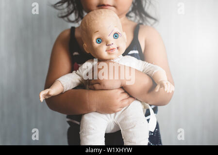 Little asian girl hugging her favourite poupée crasseux usés. Concept de l'enfant solitaire, l'amour, l'enfance et la parentalité. Selective focus sur la poupée. Banque D'Images