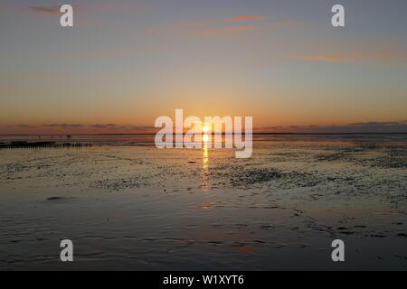 Coucher du soleil sur la mer du Nord, directement sur la plage. Ciel Orange et marée basse. Banque D'Images