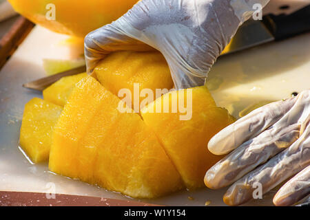 Main tenant la pastèque jaune et utiliser un couteau pour couper un morceau. Banque D'Images