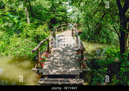 Fait main petit pont de bois sur la romantique rivière eau entouré d'arbres et de fleurs menant au quai parmi les plantes de la rivière Mad Weathered Wood Banque D'Images