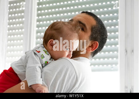 Father kissing infirmier comptable d'être parent prendre soin de bébé fille très jeune enfant nouveau-né né récemment en regardant en face de portrait Banque D'Images