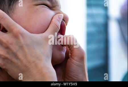 Close up image de garçon enfant enfants face grimaçante alors que les mains de la mère de l'enfant contrôle des dents et de la bouche à l'intérieur des gencives concept de prendre soin d'être parent Banque D'Images