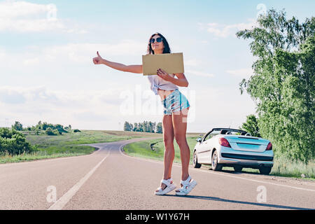 Smiling woman auto-stoppeur sur la route est holding a blank board. Concept : voyager à travers le monde, d'euros, les vacances, les gens, les vacances. Banque D'Images