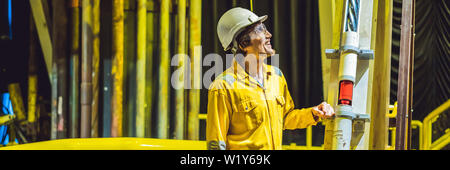 Jeune homme dans un uniforme de travail jaune, les lunettes et le casque dans un environnement industriel, plate-forme d'huile ou de gaz liquéfié, format long bannière plante Banque D'Images