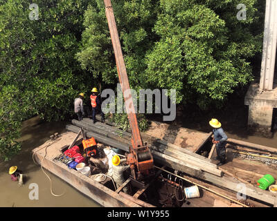 Équipe de travailleurs tirez des colonnes de béton hors de l'eau sur le fer avec ponton grue. La reconstruction de la côte du fleuve, Thaïlande Banque D'Images