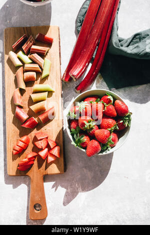 La rhubarbe et fraises fraîches coupées en morceaux sur un cutboard en bois sur une base en béton, des coups de table forte lumière directe avec de riches sh Banque D'Images