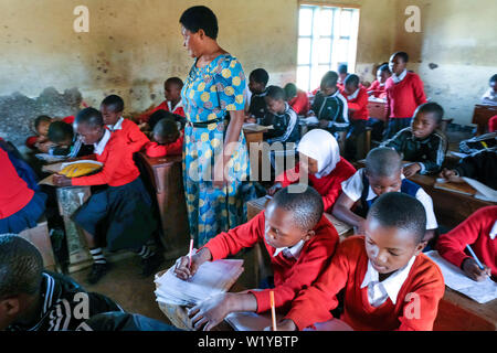 L'enseignant et les étudiants en rouge l'uniforme scolaire dans une classe d'école de l'école primaire de Mwenge à Mbeya, Tanzanie Banque D'Images