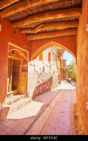 Marche à travers l'étroit passage sous la maison avec ancien log plafond et murs en adobe rouge, village Abyaneh, Iran. Banque D'Images