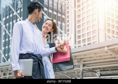 Businessman holding dollar cash avec ordinateur portable et asian woman holding Shopping bag sont heureux souriant dans la ville Banque D'Images