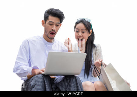 Jeune homme et femme asiatique s'asseoir à l'ordinateur portable avec enthousiaste et choqués, isolé sur fond blanc Banque D'Images