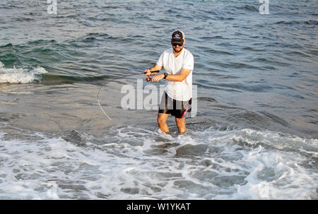 Pêcheur debout à crochets mer un poisson. Sportsman est titulaire d'une canne à pêche et le moulinet à accroché le poisson. Les prises de poissons de pêche Spin hobby à plage, Espagne, 2019. Banque D'Images