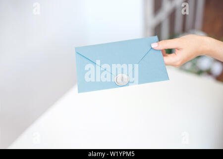 Close-up femme avec corps mince tenant dans les mains le carton d'invitation de forme carrée couleur bleu carte enveloppe Banque D'Images