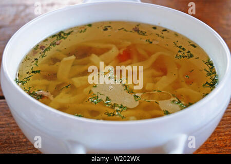 Nouilles soupe carottes et assaisonné de verts dans une assiette blanche sur une table en bois Banque D'Images