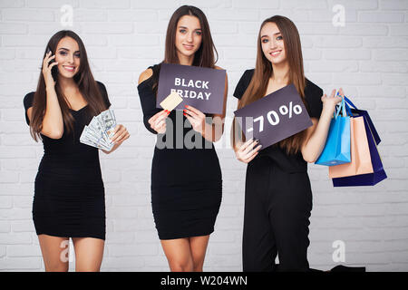 Le Shopping. Trois femmes tenant des sacs colorés sur fond clair en noir vendredi maison de vacances Banque D'Images