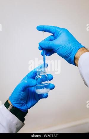 Homme ou femme les mains dans les gants de tenir les mains en tube de test produit test de l'expérience de la chimie moderne et de la recherche en laboratoire de chimie. Chemist Banque D'Images