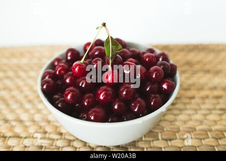 Une assiette pleine de cerises fraîches sur une serviette en osier naturel de fruits de saison. Banque D'Images