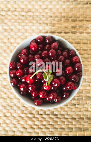 Une assiette pleine de cerises fraîches sur une serviette en osier naturel de fruits de saison. Banque D'Images